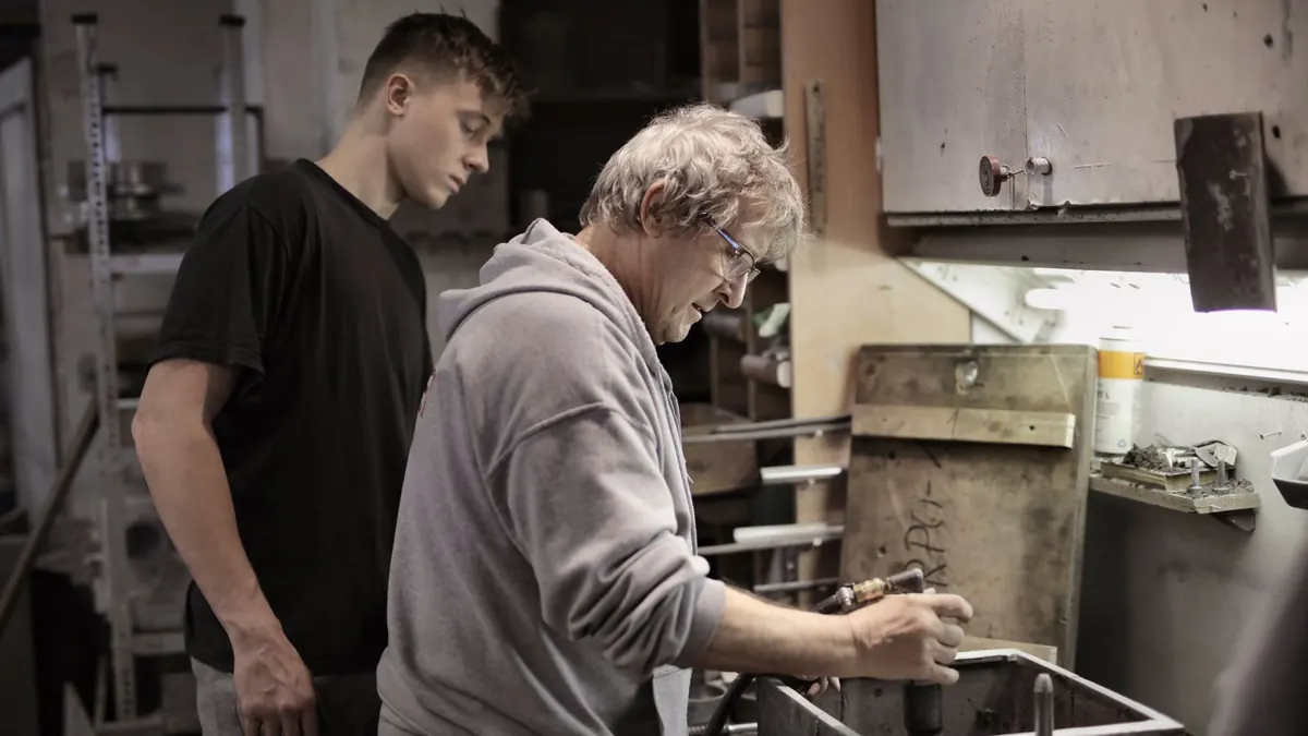 Ausbilder zeigt einem jungen Auszubildenden in der Werkstatt einen Arbeitsschritt