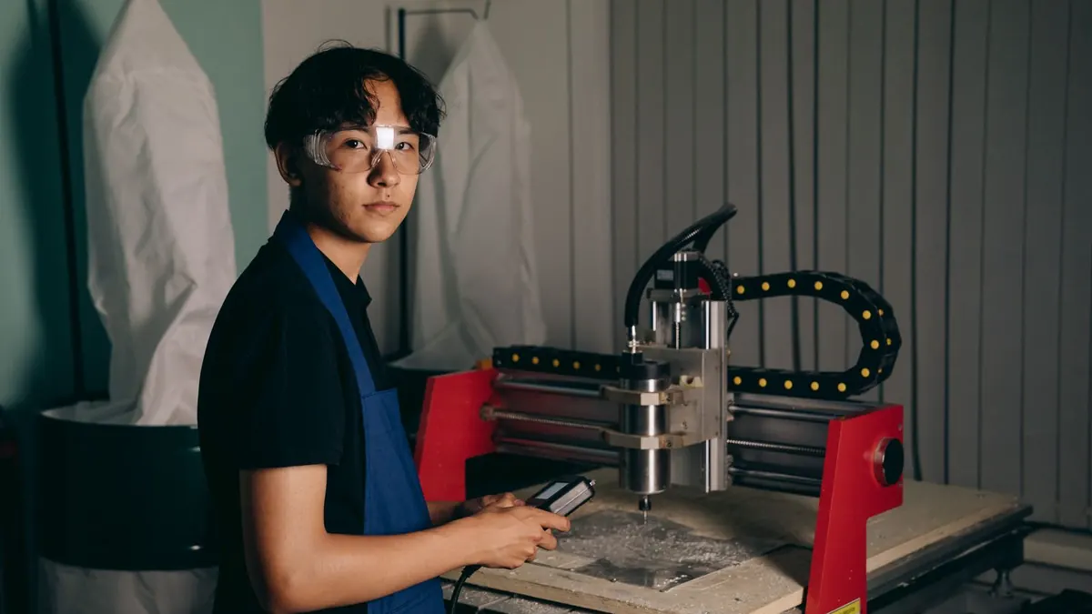 Auszubildender bedient in einer Werkstatt eine Fräsmaschine mit Schutzbrille