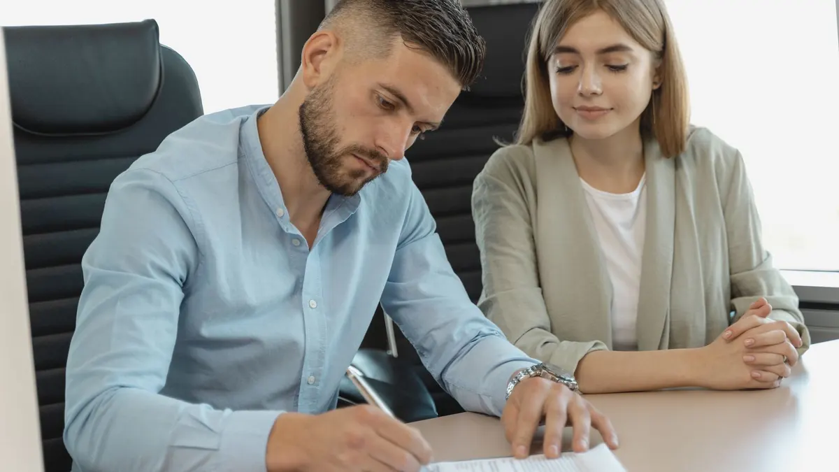 Mann und Frau unterschreiben gemeinsam Unterlagen an einem Bürotisch