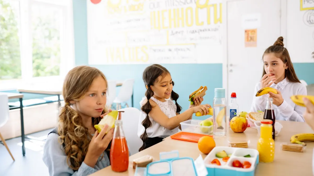 Kinder essen gemeinsam ihr mitgebrachtes Mittagessen an einem Tisch in der Schule