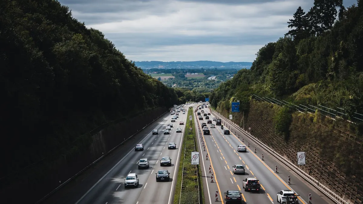 Autobahn mit dichtem Verkehr zwischen bewaldeten Hängen unter bewölktem Himmel