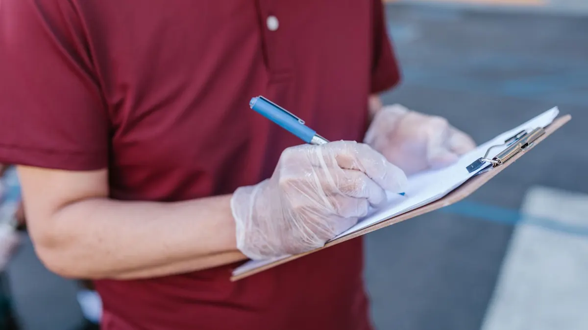 Person mit Einmalhandschuhen hakt eine Liste auf einem Klemmbrett ab