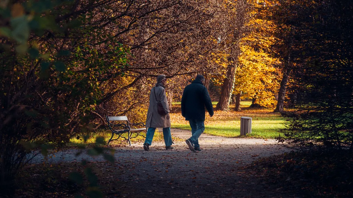 Zwei Spaziergänger gehen an einem Herbstabend durch einen Park