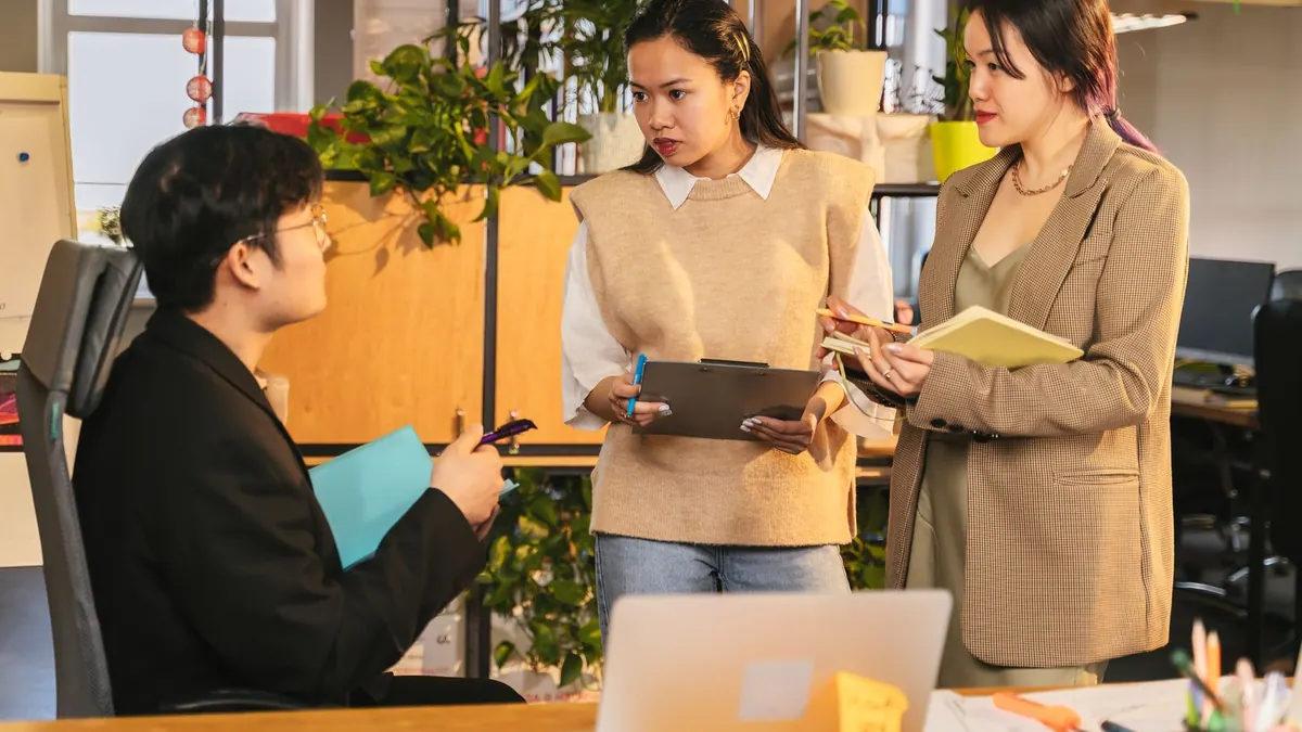 Drei Kollegen besprechen im hellen Büro Unterlagen und Notizen