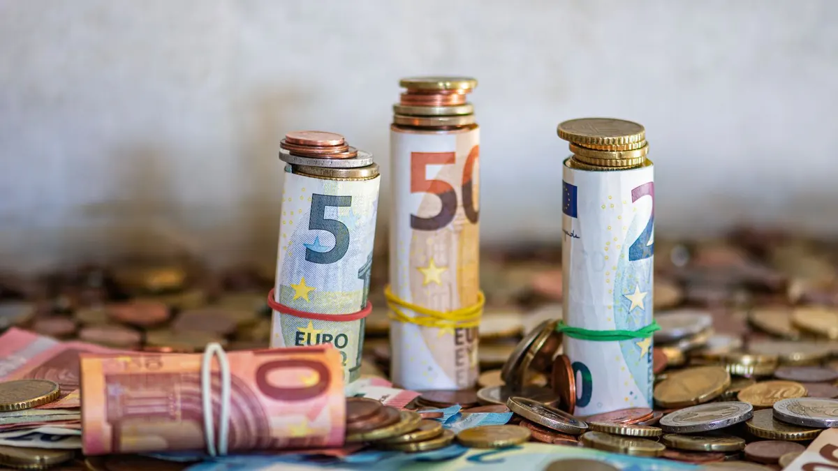 Gerollte Euro-Münzen und Geldscheine liegen gestapelt auf einem Tisch