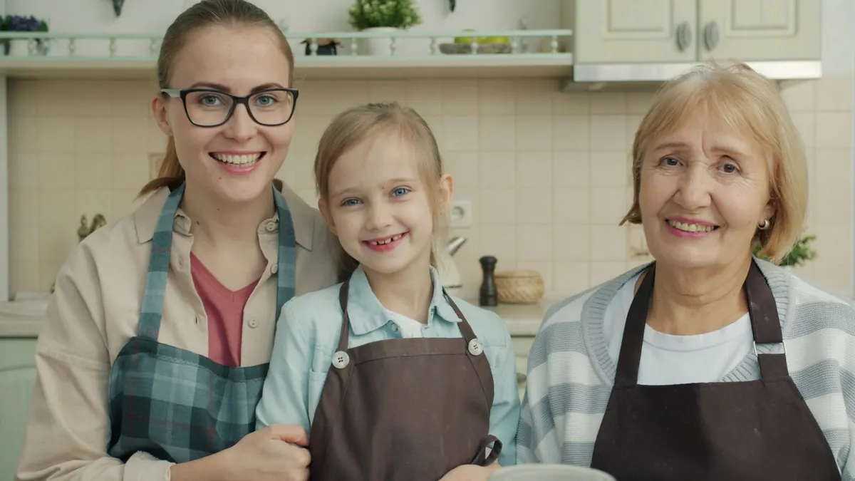Mutter, Tochter und Großmutter in Küchenschürzen lächeln gemeinsam in die Kamera