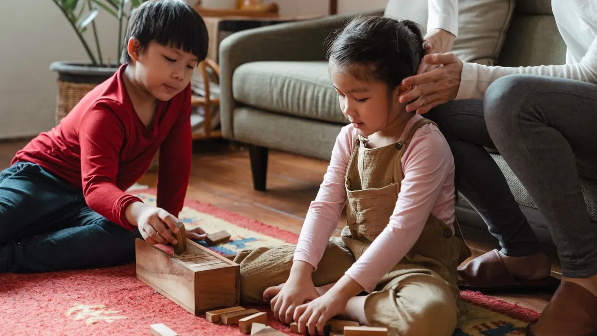 Zwei Kinder spielen auf dem Wohnzimmerteppich mit Bauklötzen und Spielzeug