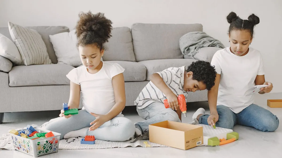 Drei Kinder spielen auf einem hellen Wohnzimmerteppich vor dem Sofa