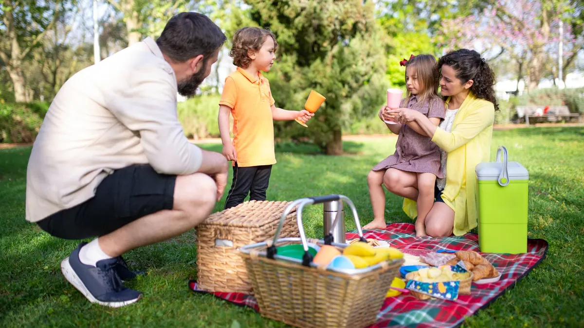Familie mit Kindern sitzt bei einem Picknick auf einer grünen Wiese