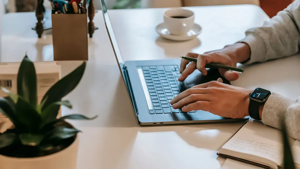 Hände tippen auf einem Laptop neben einer Kaffeetasse und einer Pflanze