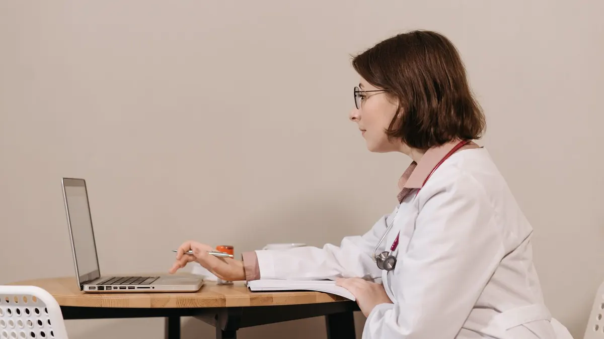 Ärztin sitzt am Tisch und arbeitet seitlich an einem Laptop