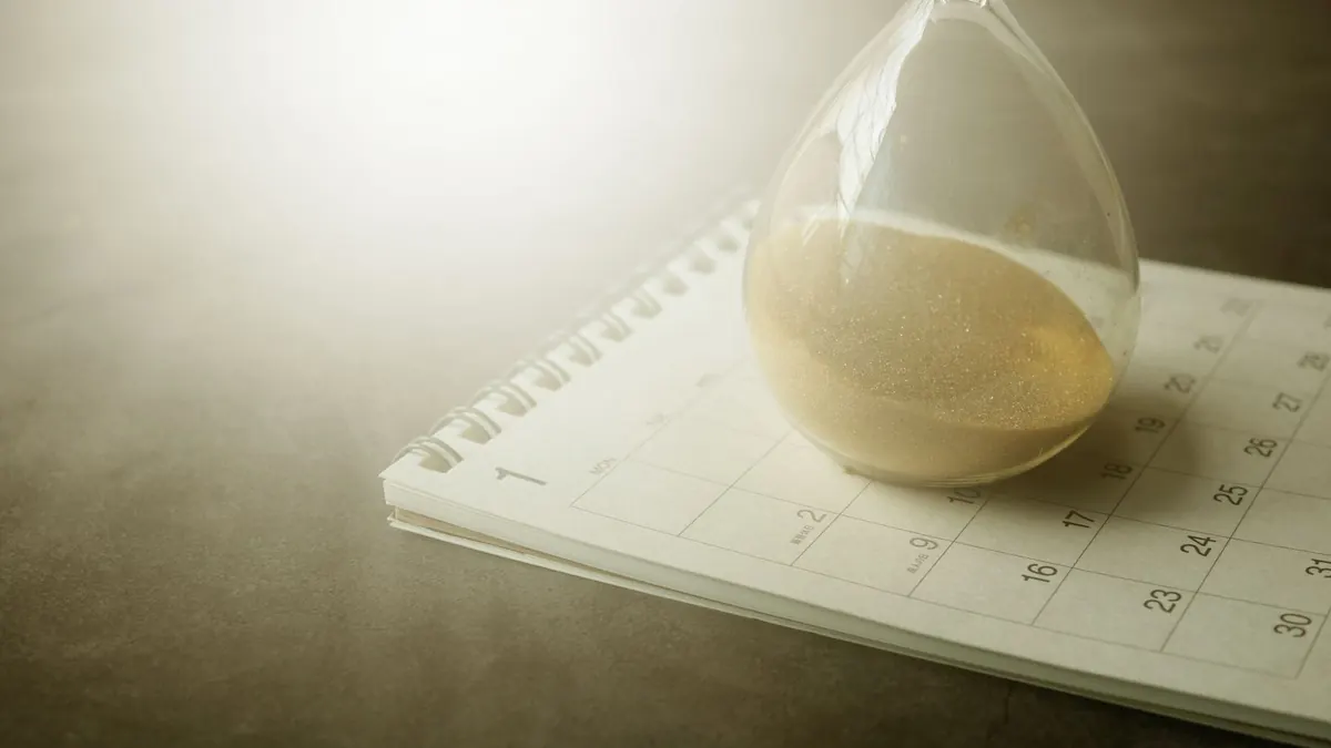 Sanduhr steht auf einem aufgeschlagenen Kalender im warmen Licht