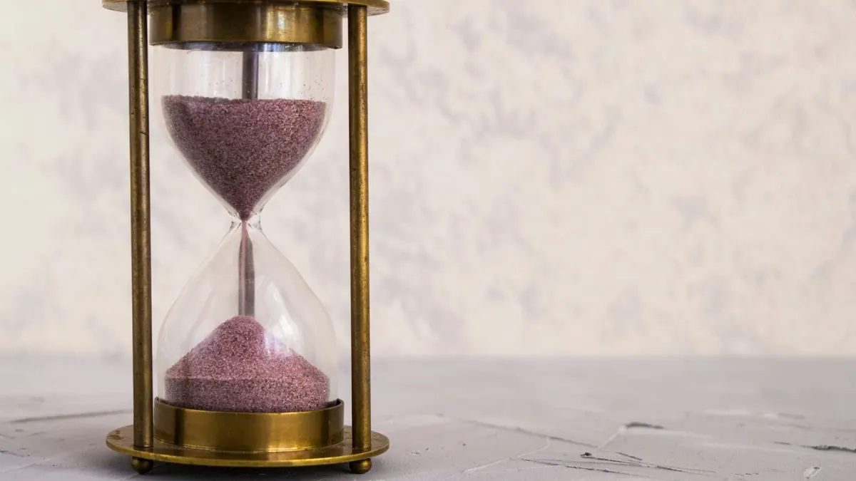 Sanduhr mit rosafarbenem Sand steht auf einem hellen Untergrund