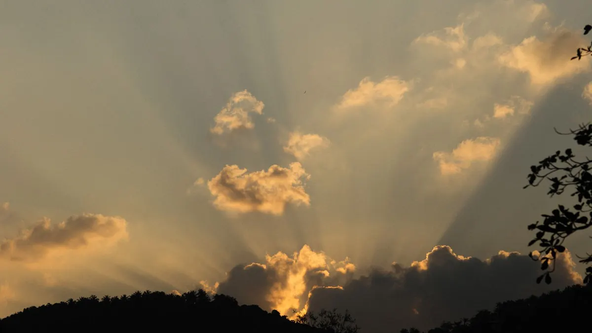 Sonnenstrahlen brechen hinter goldenen Wolken über einem Hügel hervor