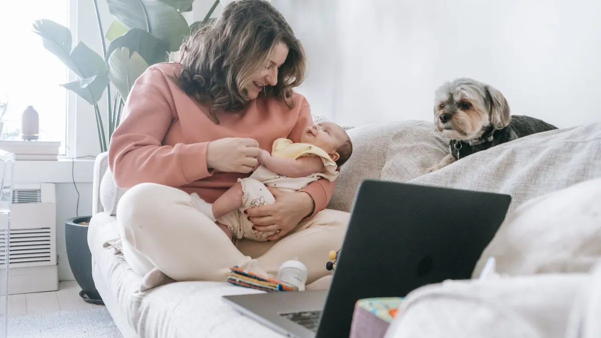 Mutter hält ihr Baby auf dem Sofa, daneben liegt ein Laptop