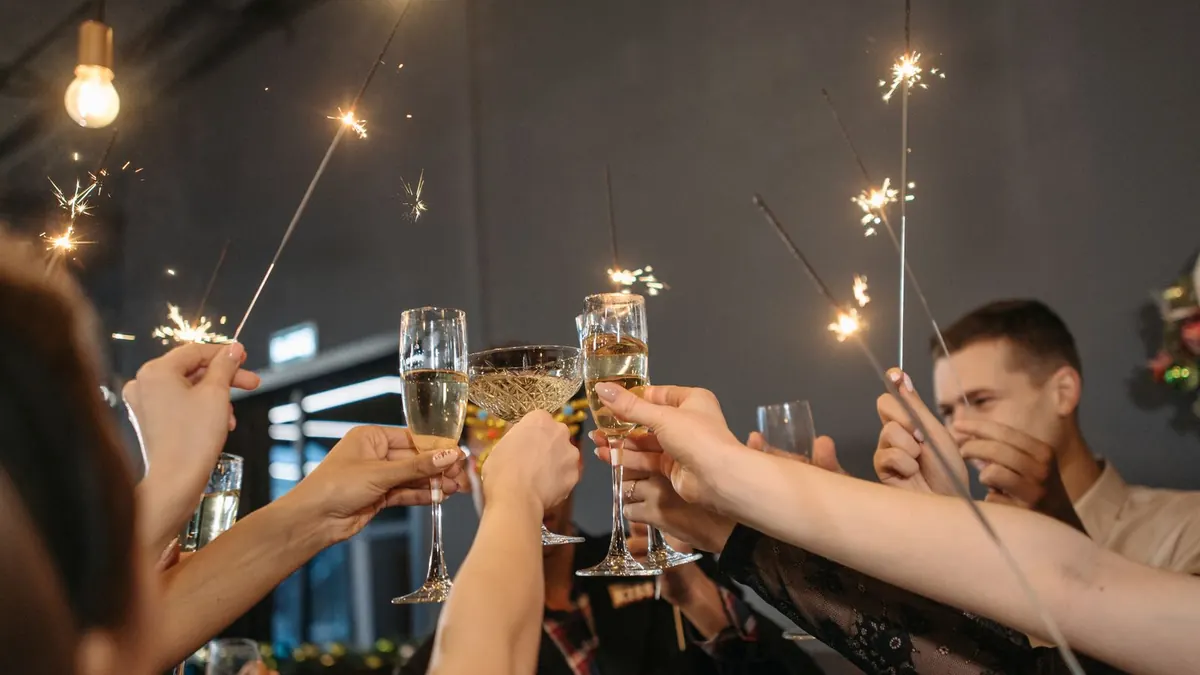 Menschen stoßen mit Sektgläsern an und halten Wunderkerzen in der Hand