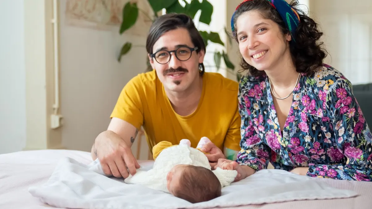 Glückliches Elternpaar liegt mit seinem Neugeborenen auf einem Bett