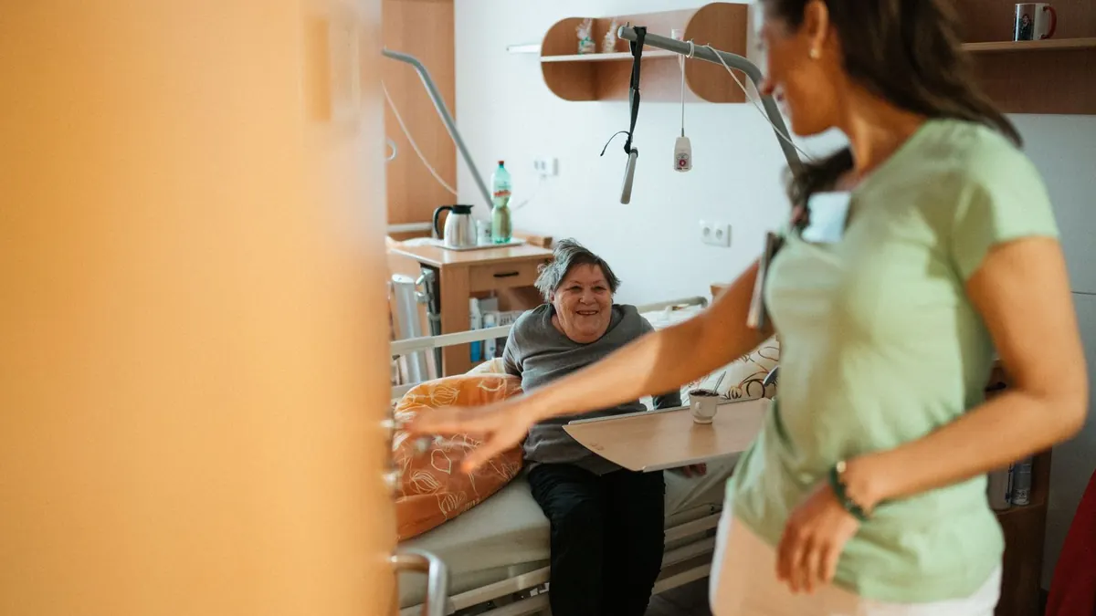 Pflegekraft hilft in einem Pflegezimmer freundlich einer älteren Person