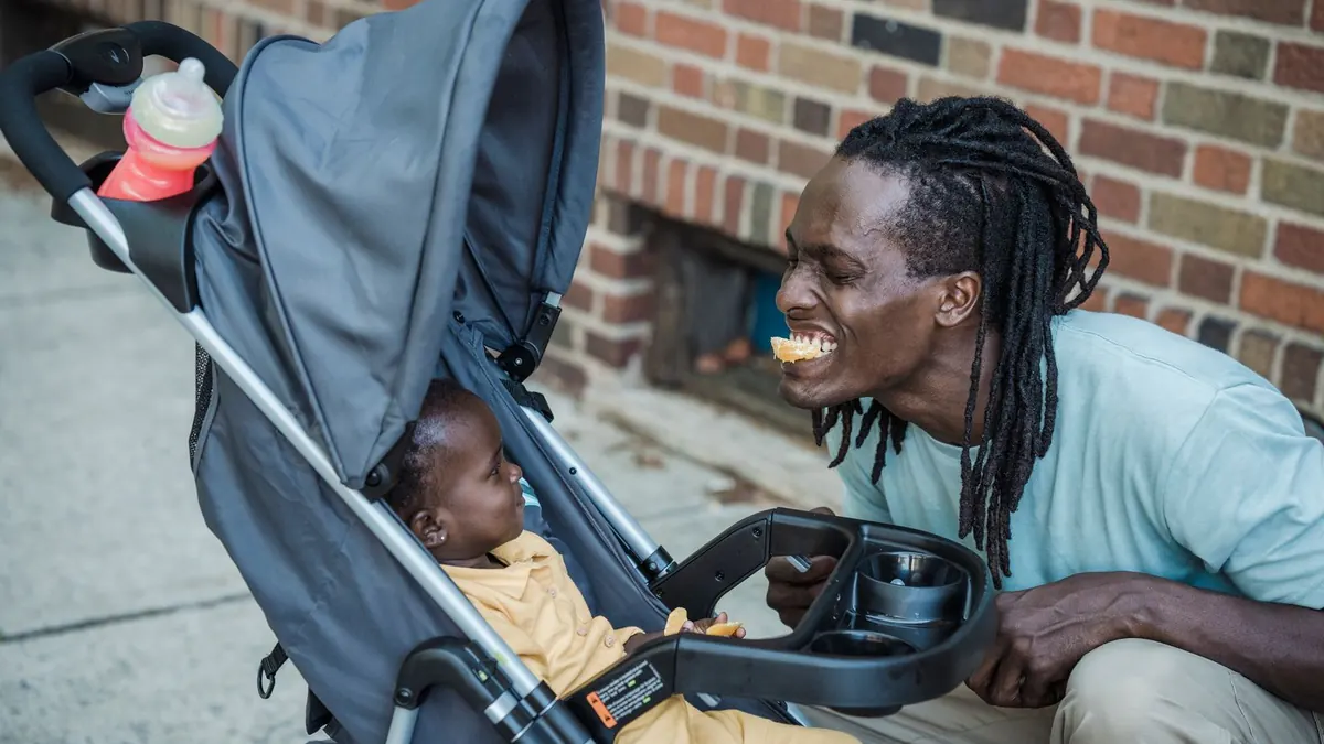 Vater lacht seinen Sohn im Kinderwagen auf einer Straße an