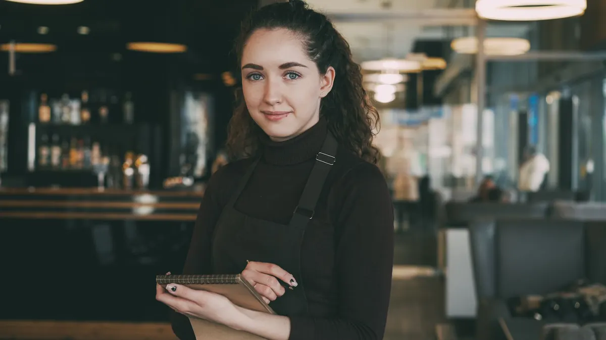 Junge Frau in Schürze hält in einem Café einen Notizblock