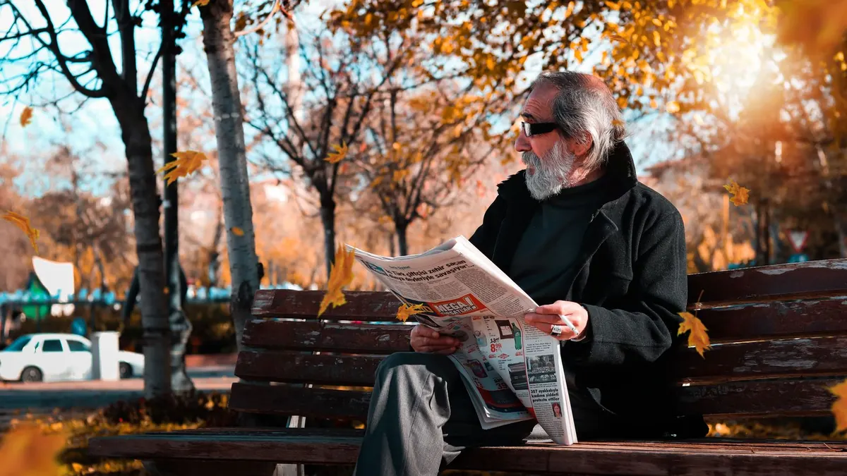 Rentner liest im Herbst auf einer Parkbank in der Sonne Zeitung
