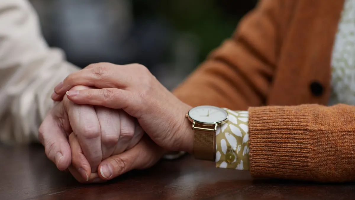 Zwei ineinandergelegte Hände von Senioren mit Armbanduhr auf einem Tisch