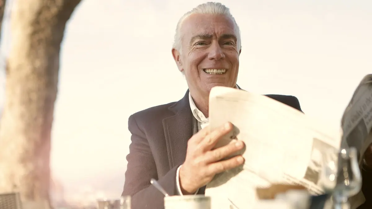 Älterer Mann lacht beim Zeitunglesen in einem sonnigen Café
