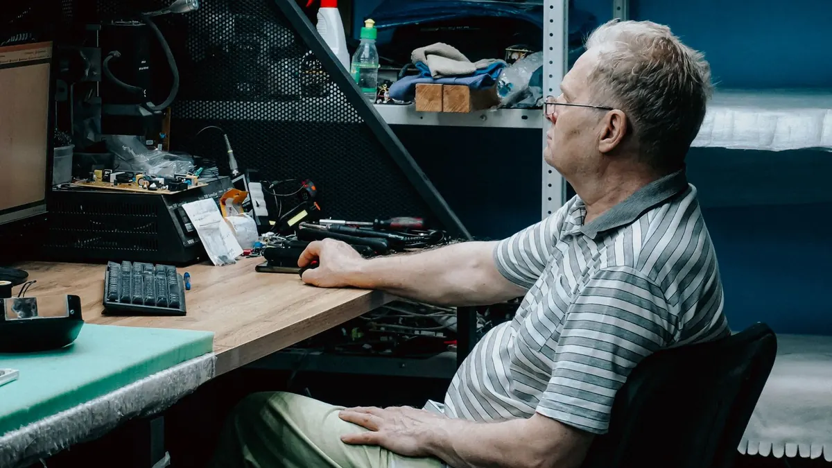 Älterer Mann arbeitet in einer Werkstatt am Schreibtisch mit Elektronik