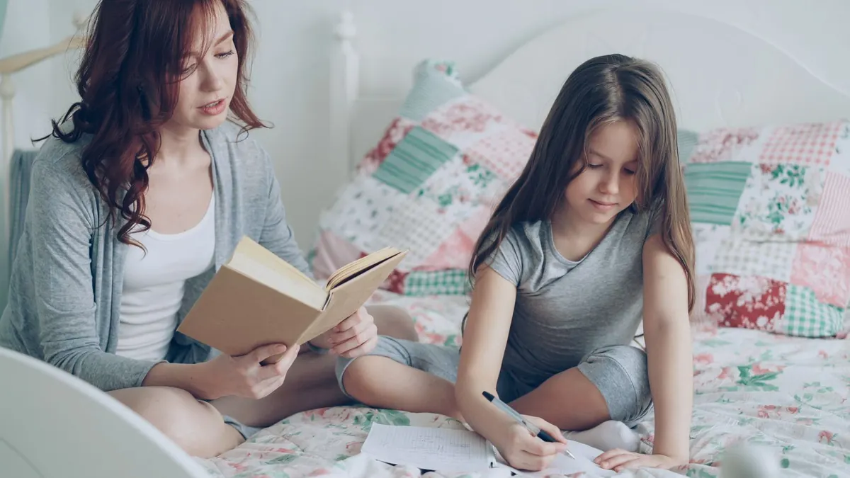 Mutter liest einem Mädchen auf dem Bett ein Buch vor
