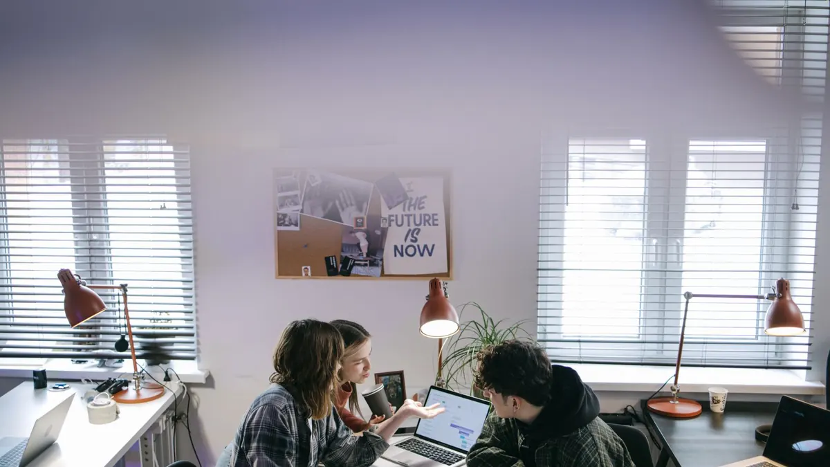Drei Personen arbeiten in einem hellen Büro konzentriert an Laptops