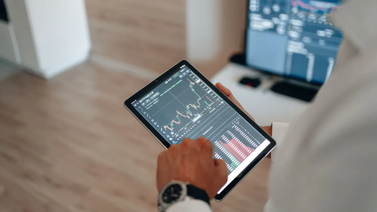 Hand hält ein Tablet mit Kurscharts in einem hellen Raum