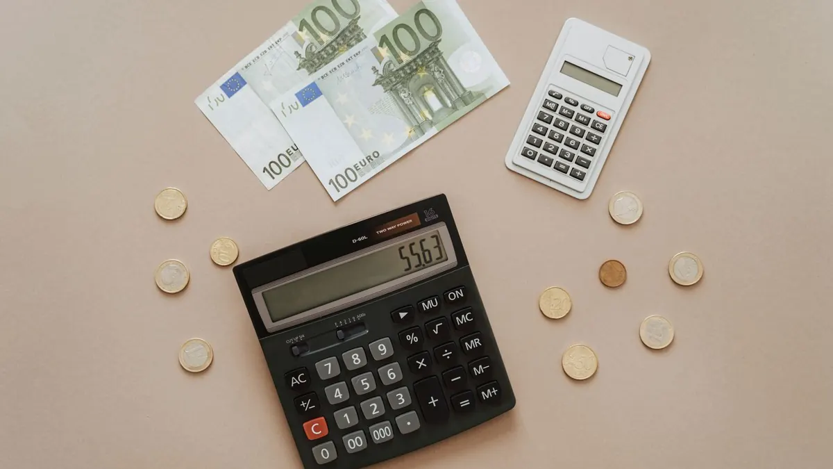 Euroscheine, Münzen und Taschenrechner liegen auf beigem Untergrund