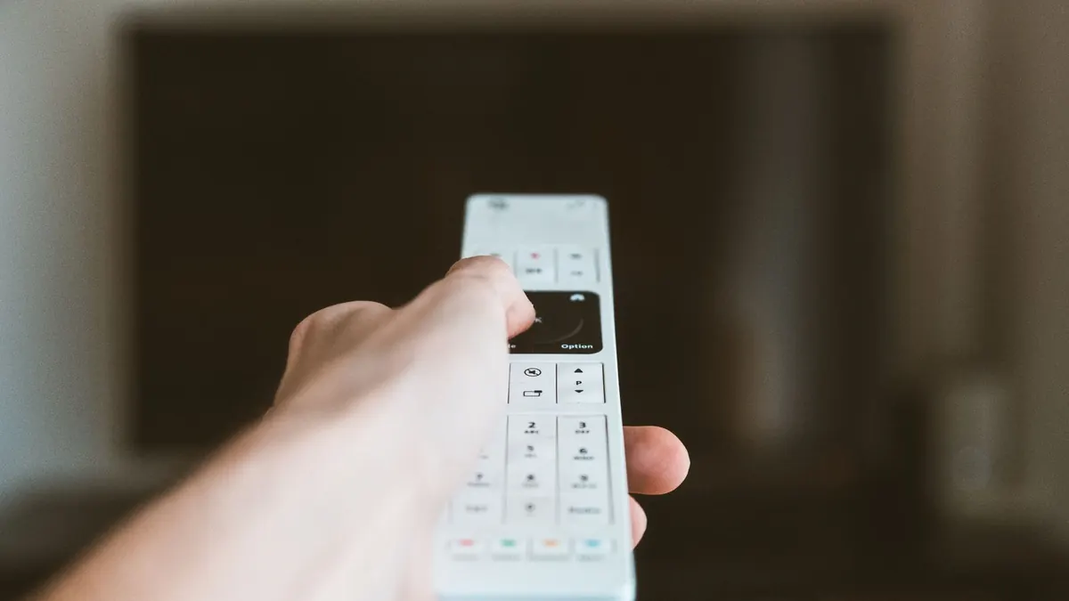 Hand hält eine Fernbedienung vor einem dunklen Fernseher