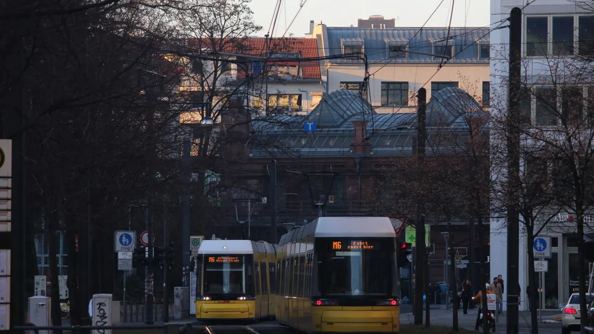 Gelbe Straßenbahnen fahren am Abend durch eine Stadt vor Altbauten