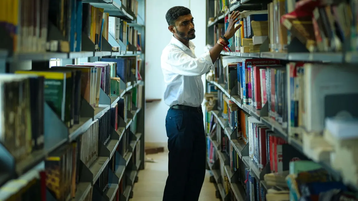 Mann sucht zwischen hohen Regalen einer Bibliothek nach einem Buch