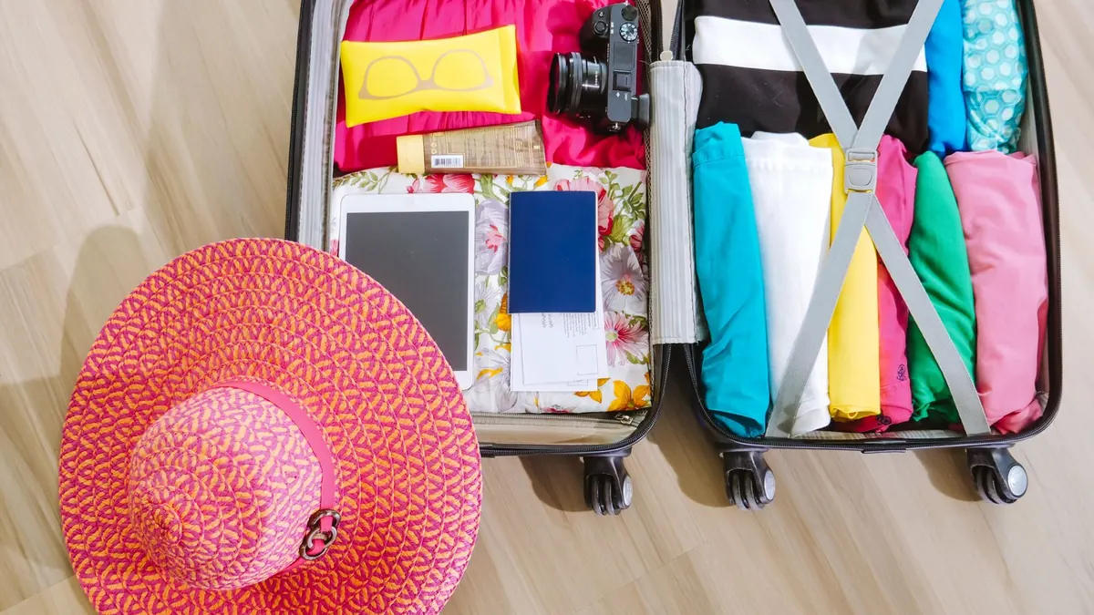 Geöffneter Koffer mit Kleidung und rotem Sonnenhut vor der Urlaubsreise