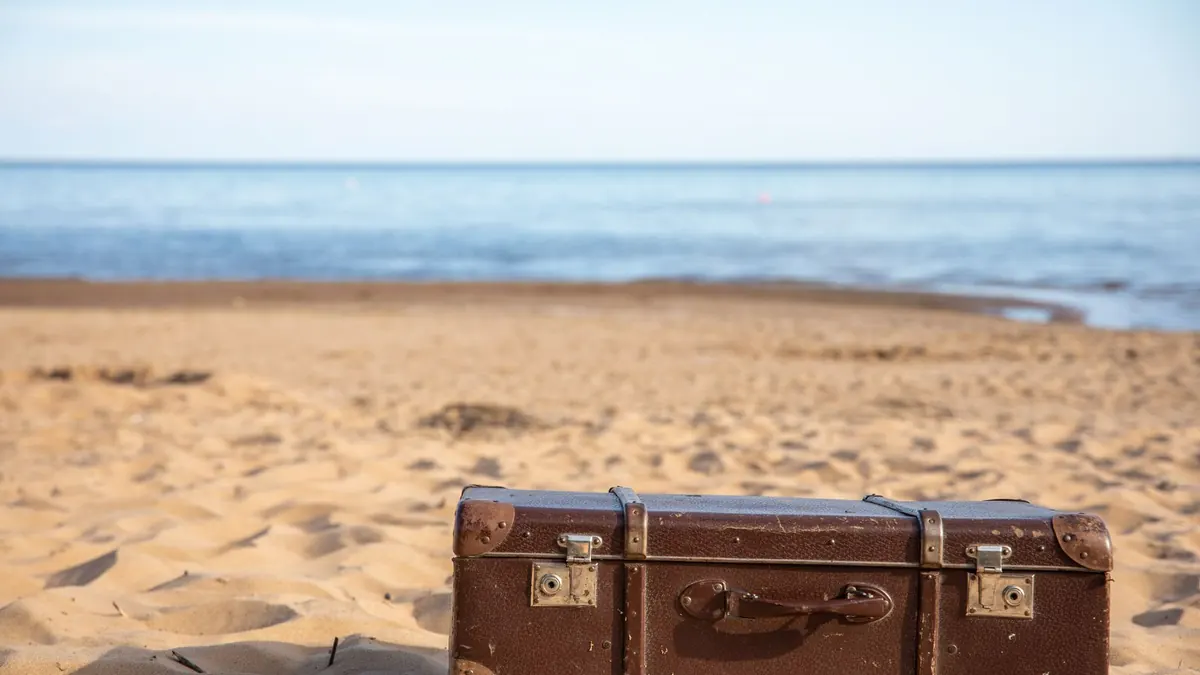Alter Koffer steht am Sandstrand vor dem ruhigen Meer
